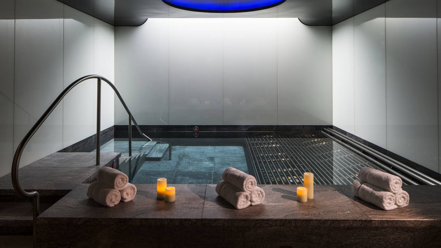 Rolled white towels, candles on spa vitality pool ledge under blue dome ceiling