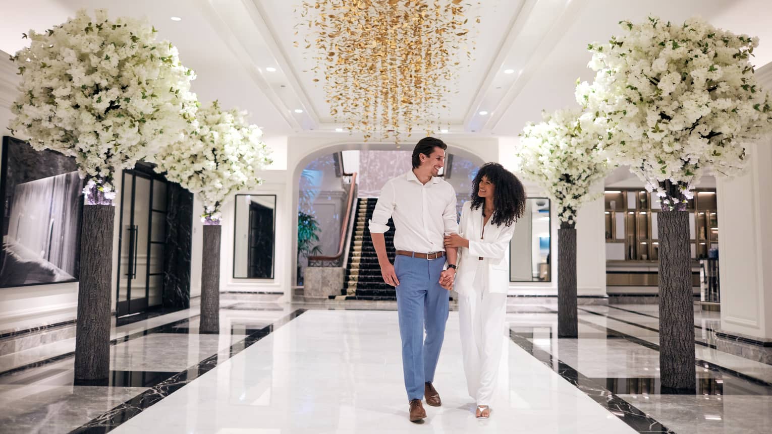 A man and woman walking down a large hall with flowers on both sides.
