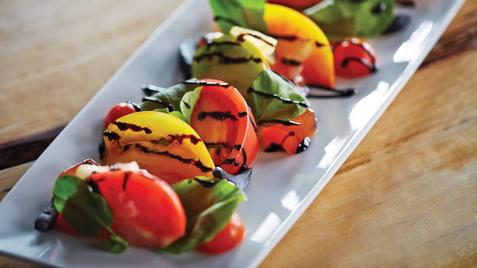 Plated wedges of yellow and red tomatoes garnished with fresh basil and balsamic vinegar
