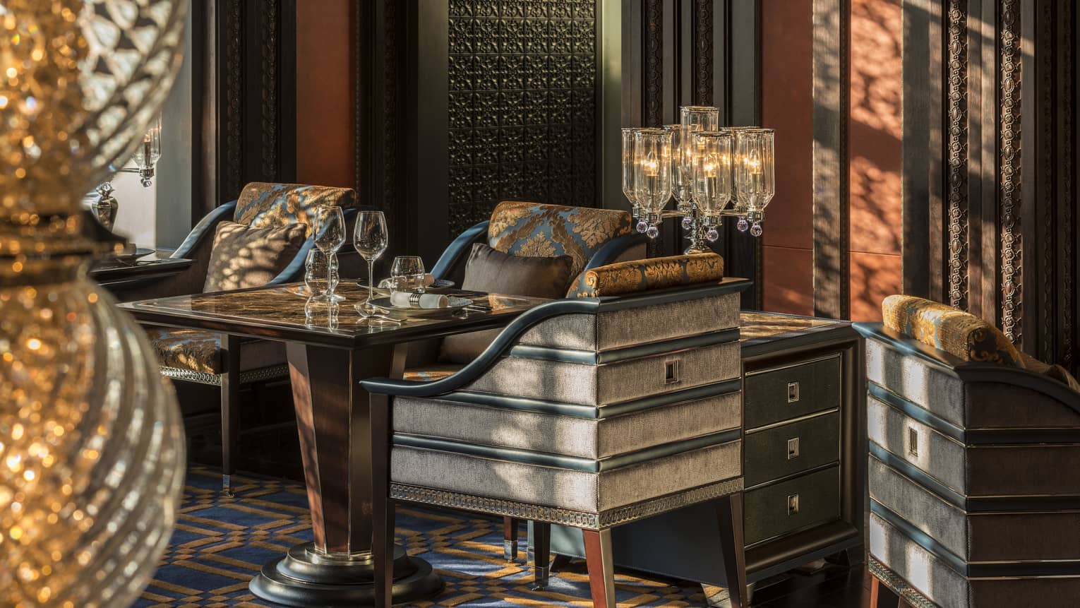 Close-up of elegant grey upholstered dining chair with blue-and-gold cushions around table with wine glasses