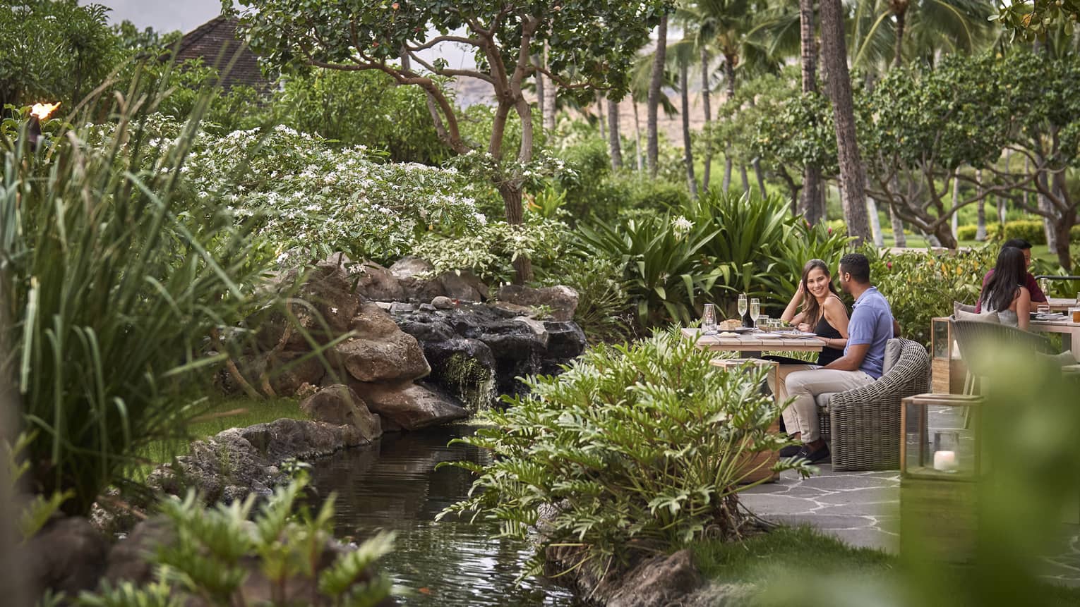 Couple sitting at table surrounded by lush greenery at contemporary outdoor restaurant