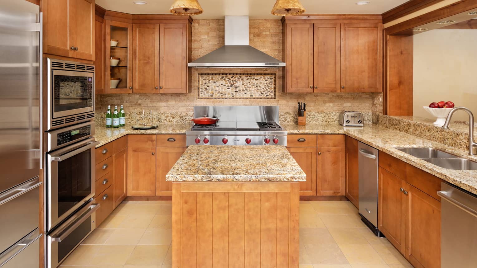 Kitchen with granite countertops, stainless steel appliances, wood cabinets, an island and a decorative stone backsplash under the range hood