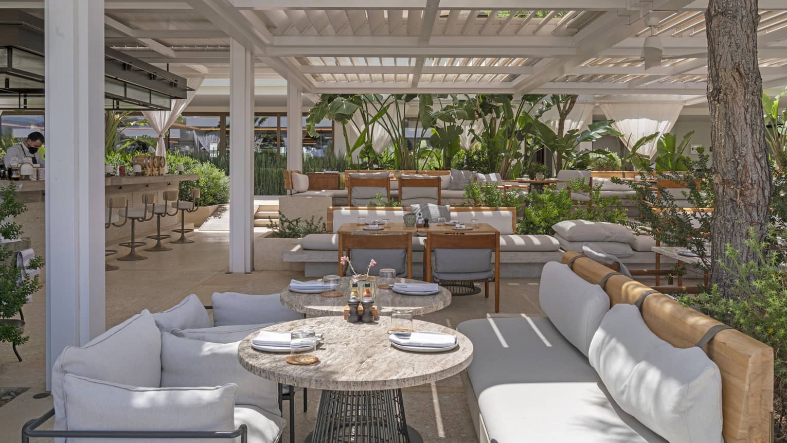 Helios restaurant's terrace with pergola, casual banquette seating, lush greenery and spacious bar
