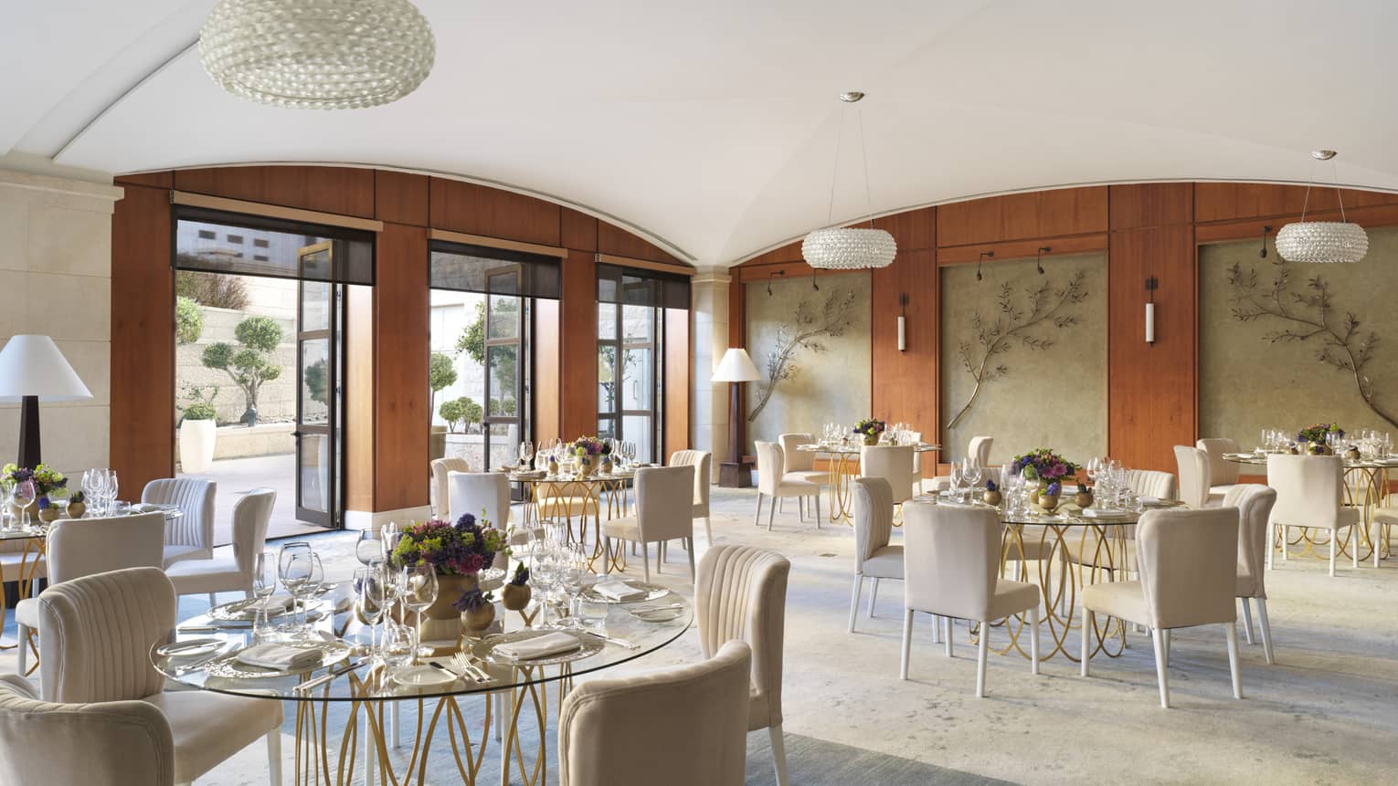A large cafe with leaf decor on the walls, and several glass tables surrounded by cream coloured chairs.