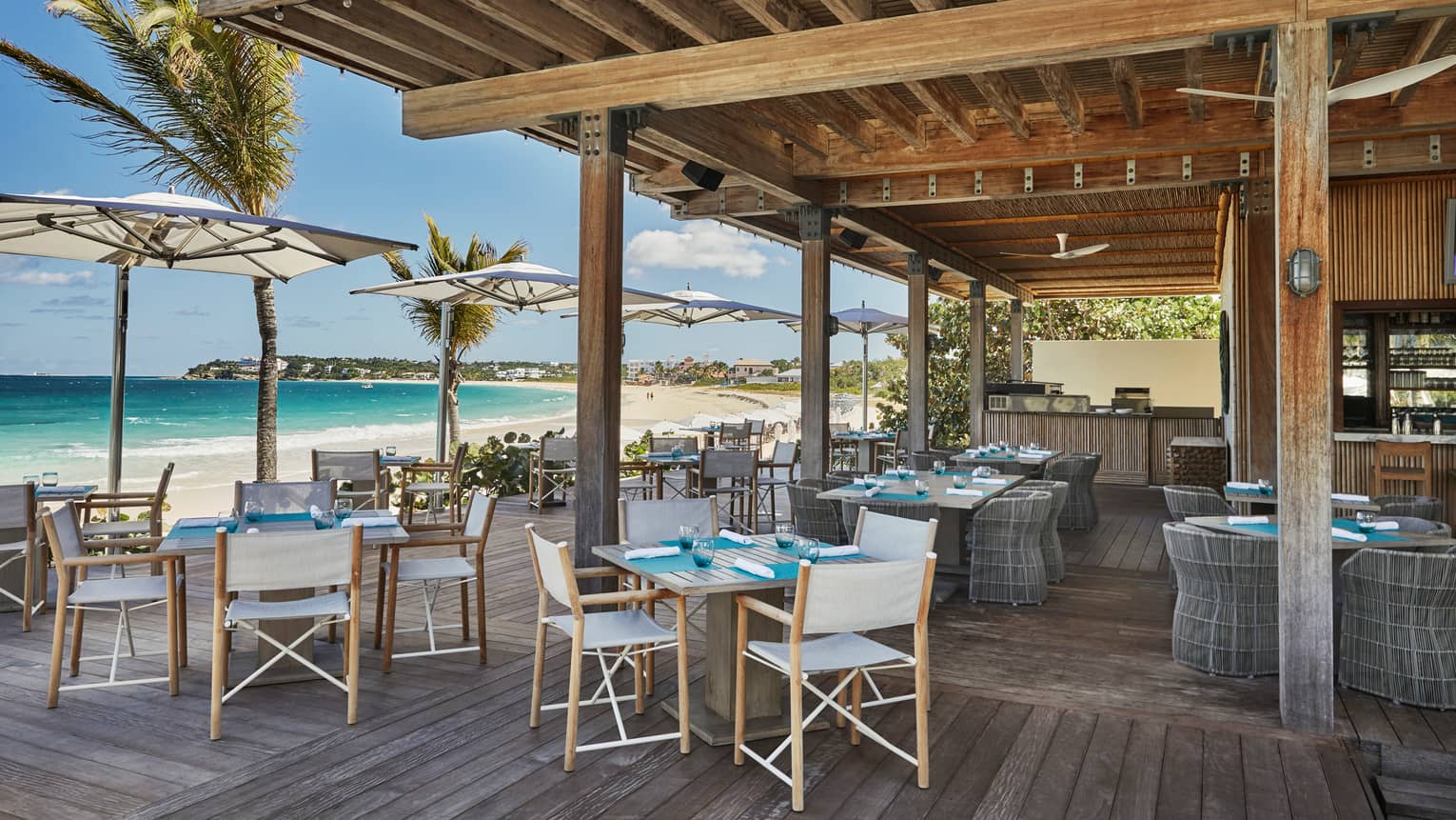 Bamboo restaurant outdoor patio, tables and chairs under wood pergola, beside sunny beach