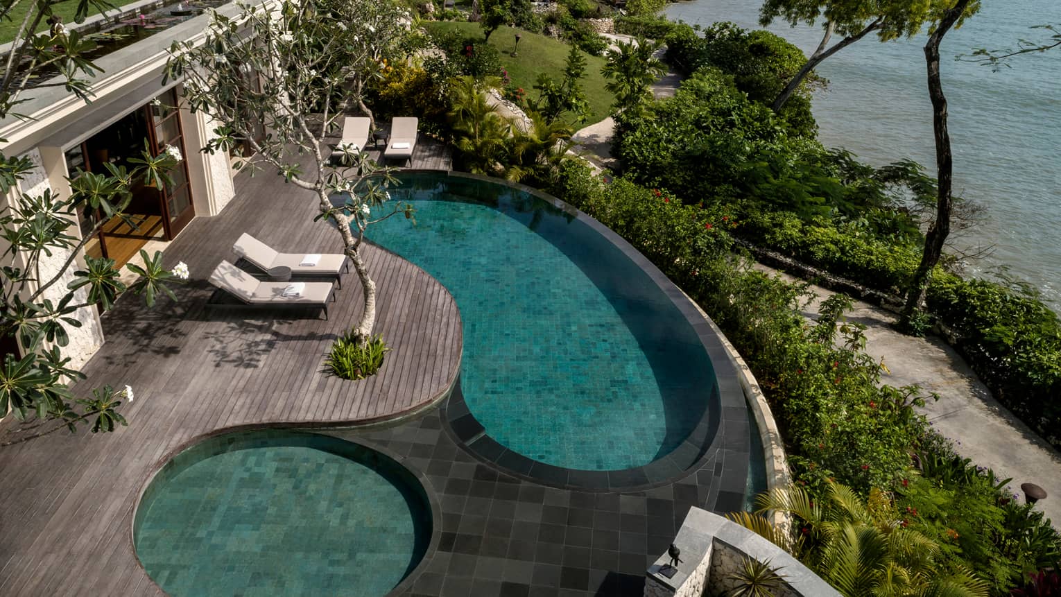 Looking down at Imperial Villa swimming pool and whirlpool on deck with white lounge chairs, garden path and ocean below