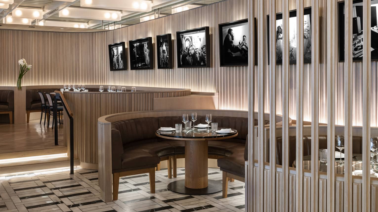 Thin, vertical panels of light-stained wood line the walls and the outside edges of curved banquet-style tables at a restaurant, with black-and-white photography hanging on the walls
