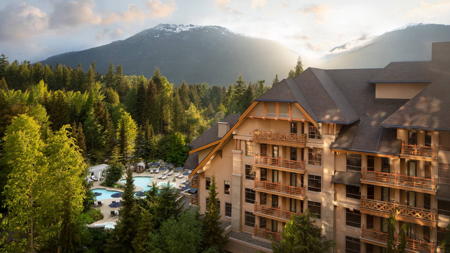 A large hotel building surrounded by mountains and trees during sunrise.