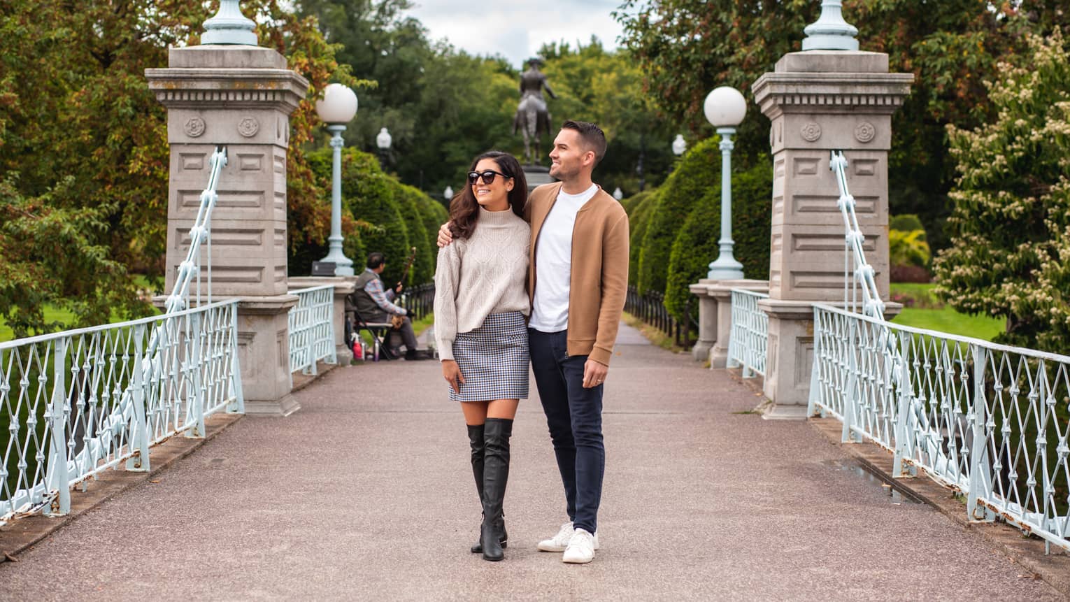 A man and woman walking along a bridge with a park behind them.