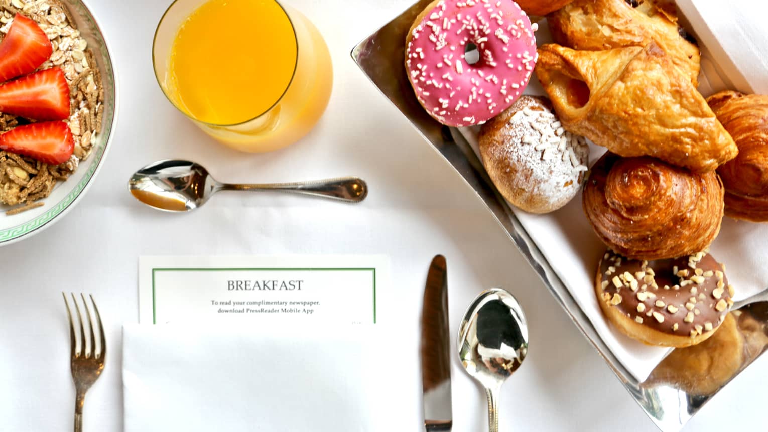 Aerial view of in-room breakfast table with menu, tray with pastries, doughnut with pink icing, orange juice