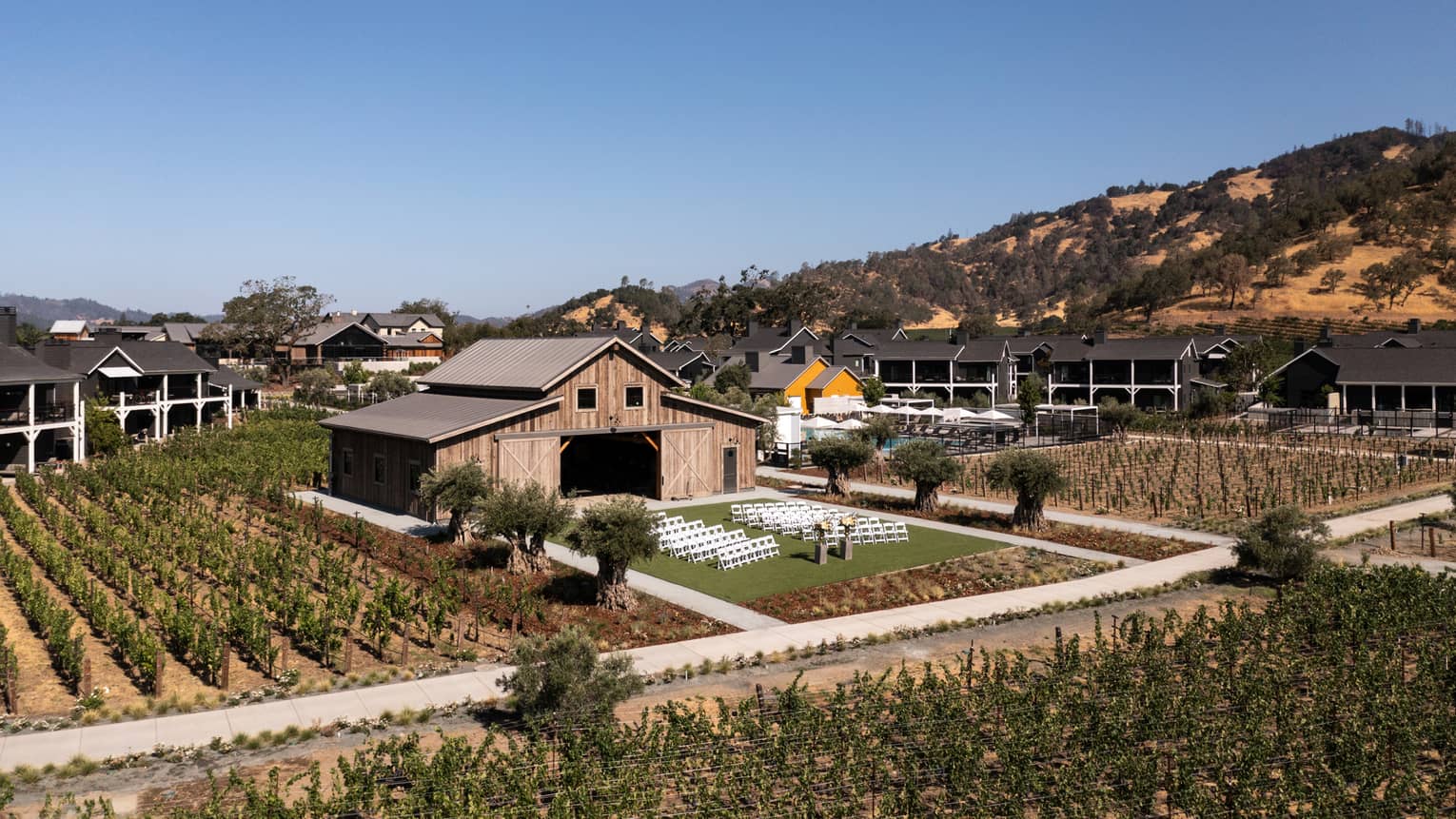 A farmhouse with mountains in the background and rows of greenery all around.