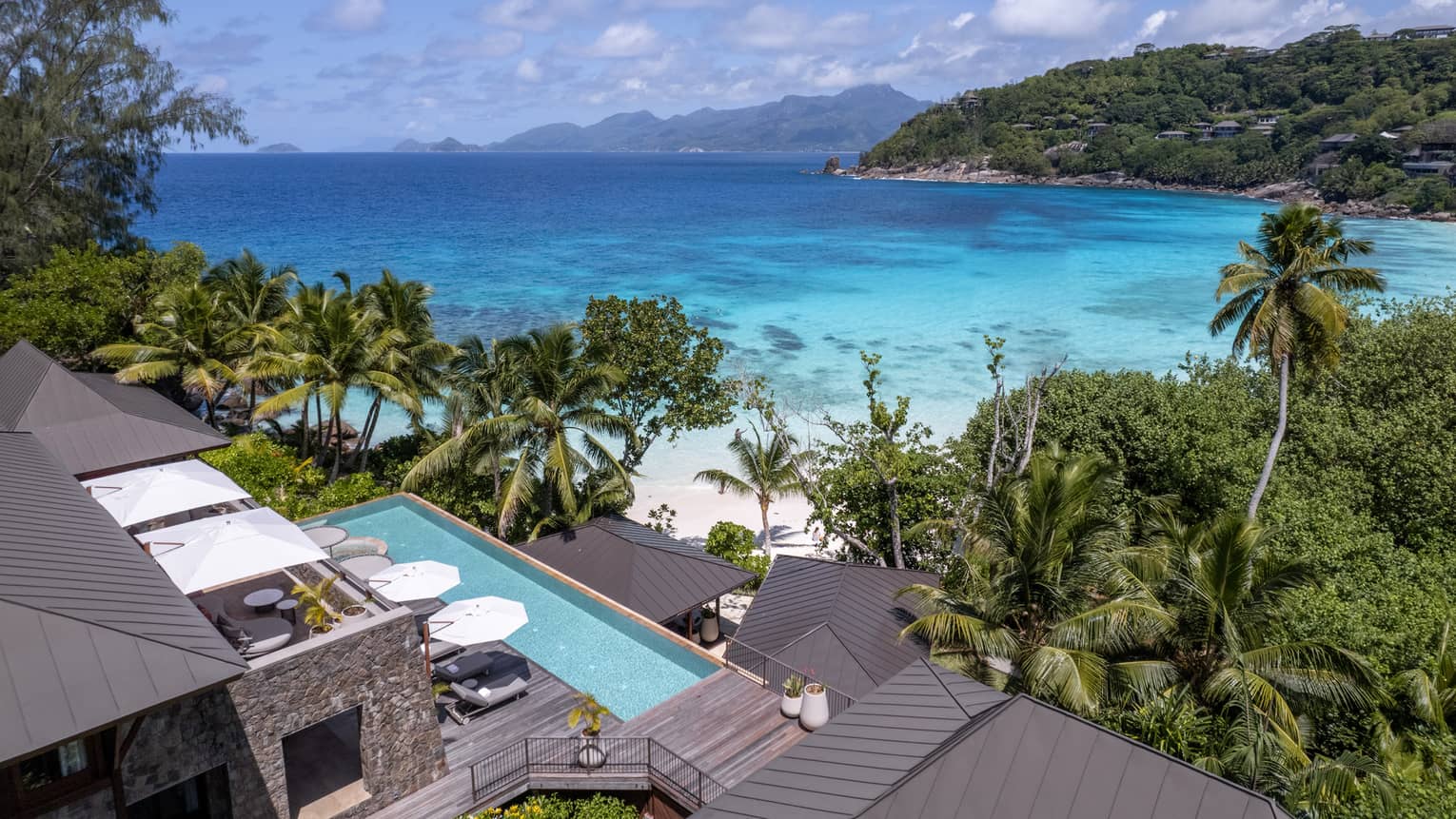 Long rectangular pool of suite in tropical setting with view of beach and lush landscaping