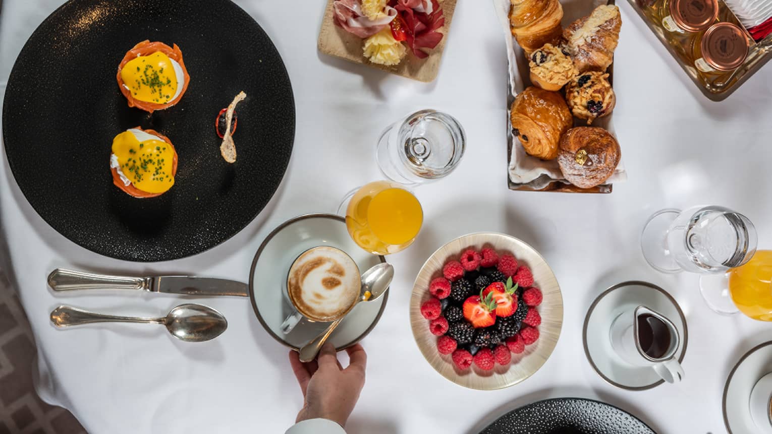 Aerial view of brunch dishes, fruit, juices, water set on white tablecloth