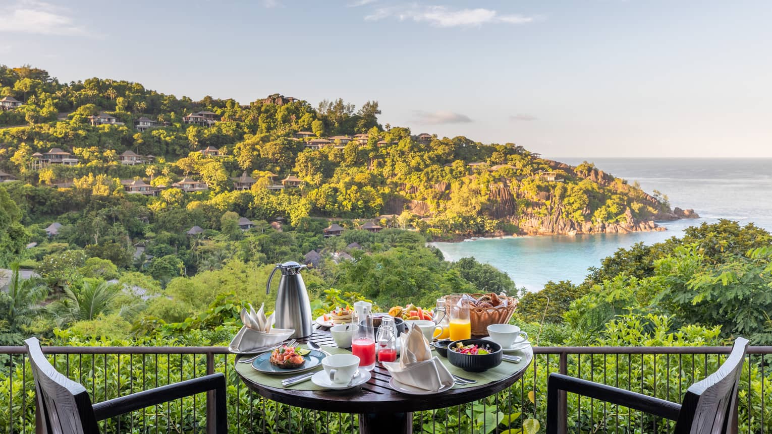 Bistro table and chairs with breakfast dishes and carafe, overlooking tropical hillsides and ocean