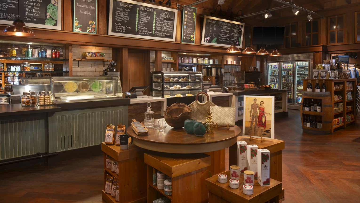 A spacious, well-lit area with warm wood decor, a counter with menus overhead and display cases of food items. There are also stocked shelves and free-standing displays of items in the space.