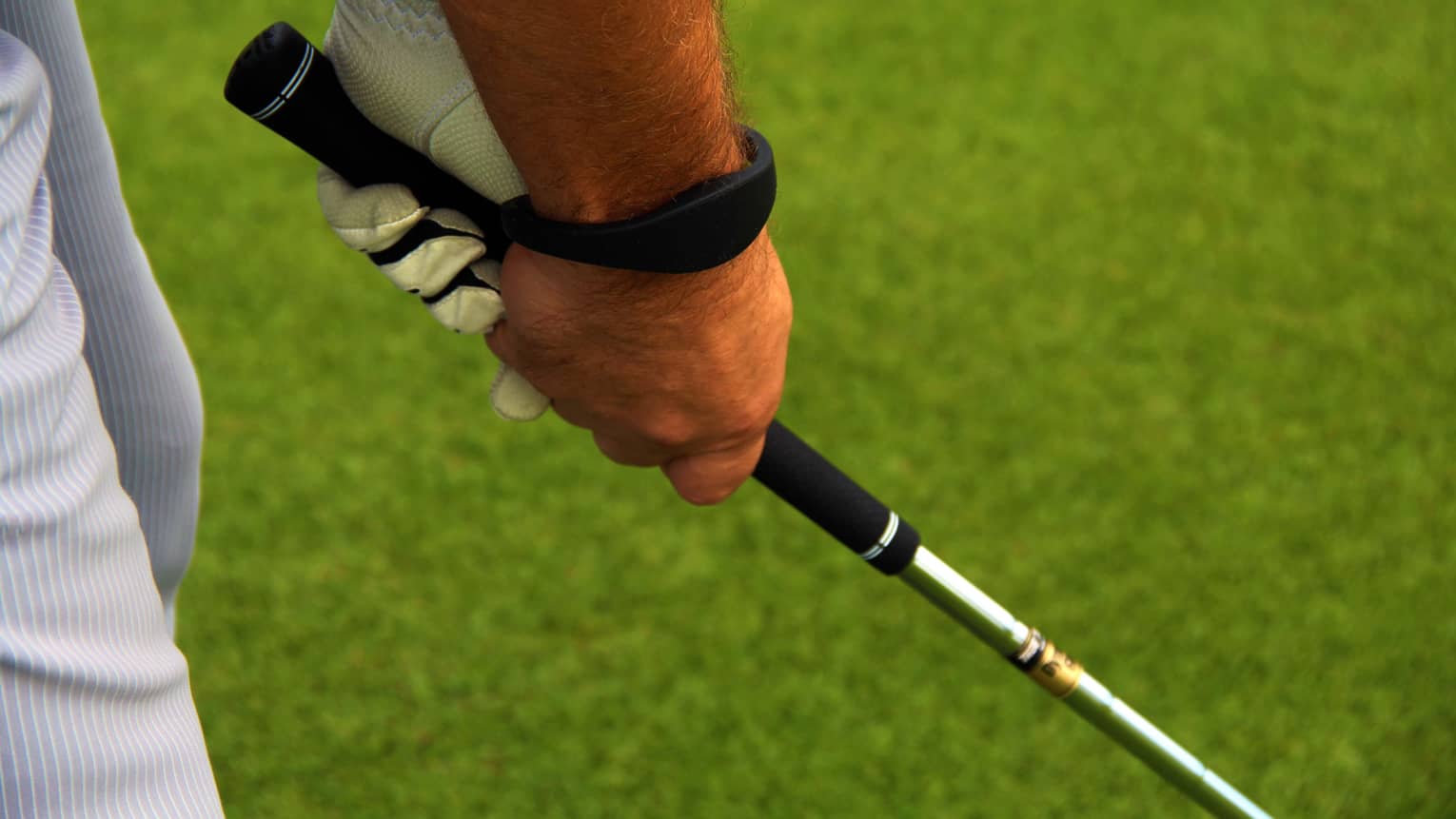 Close-up of hands gripping golf club on golf course green