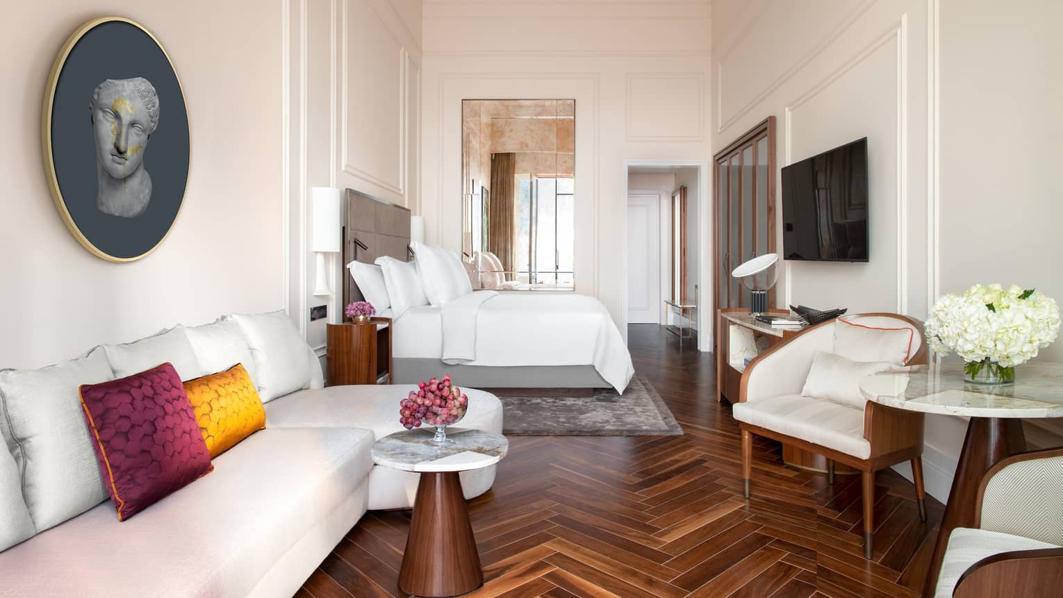 Suite with white king bed, high ceilings, wooden floors, sofa, table and two chairs