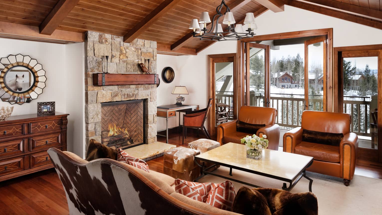 Cowhide sofa, leather armchairs. stone fireplace under arched wood beam ceiling