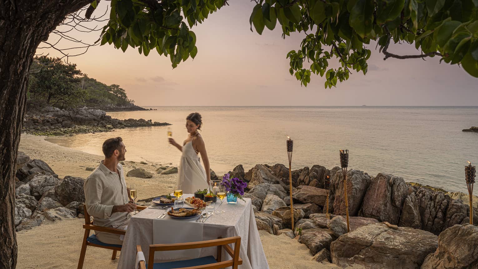A beach dinner date at dusk, with a couple enjoying a serene seaside view.