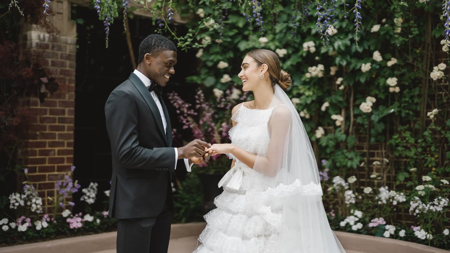 A bride and groom holding hands surrounded by brick walls and flowers.