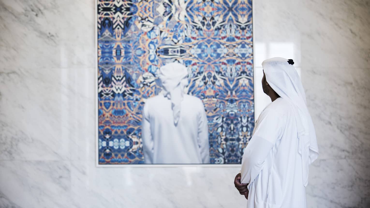 Side view of man dressed in white looking at colourful painting on white marble wall
