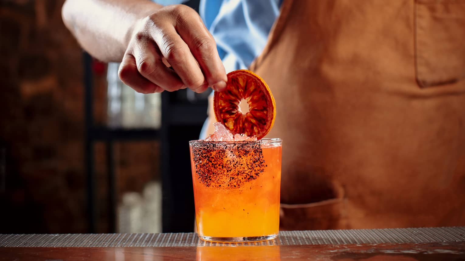 A bartender making an orange cocktail and putting a dark orange wheel in it.
