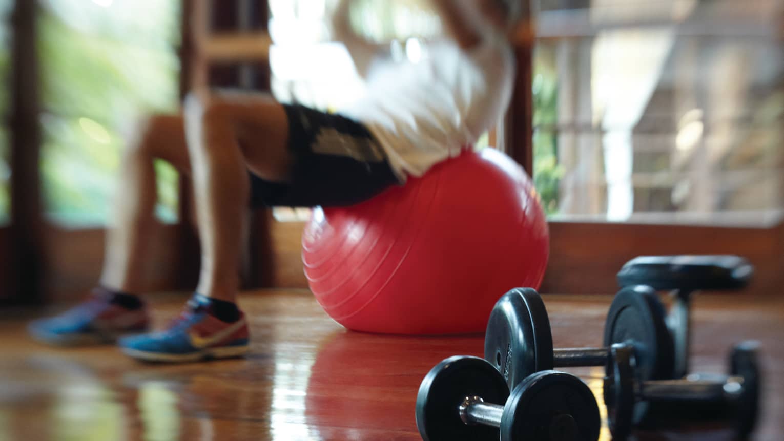 Blurry image of man in exercise clothes balancing his back on red pilates ball in Fitness Centre