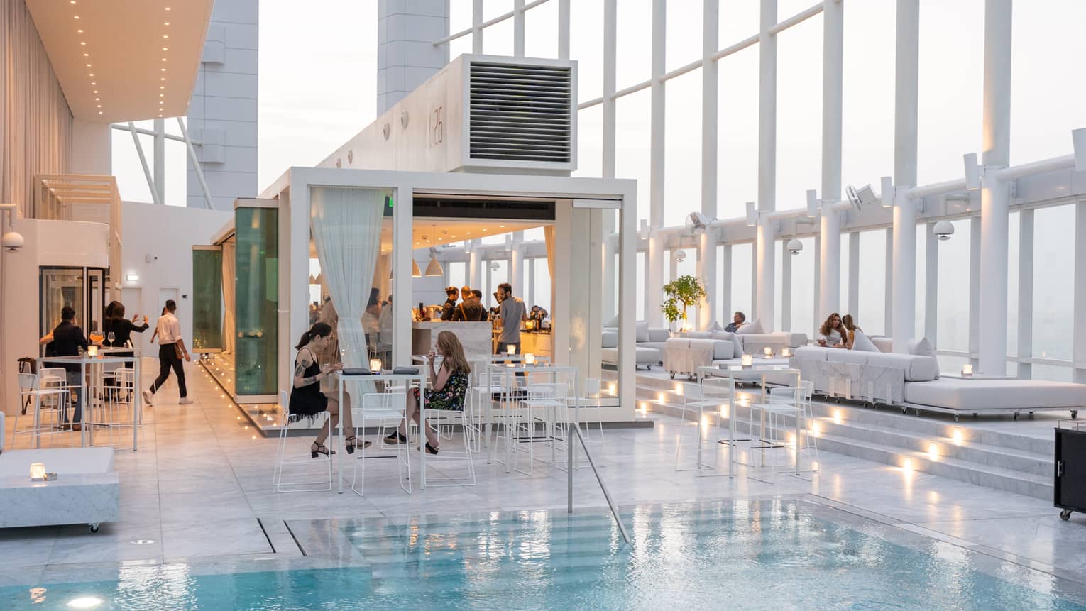 People mingle around a contemporary white bar next to pool