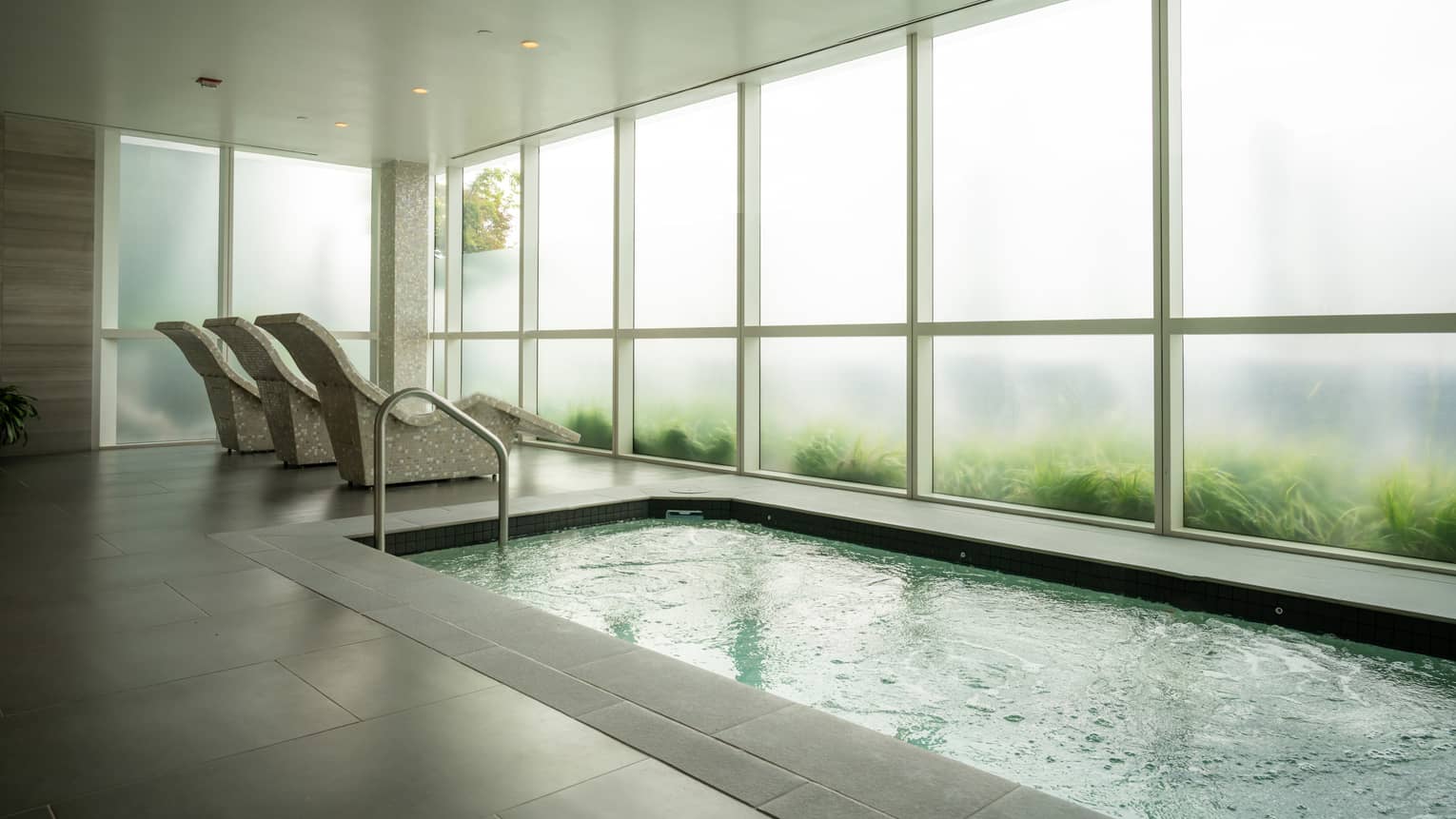 A room with three lounge chairs and a pool and floor-to-ceiling windows