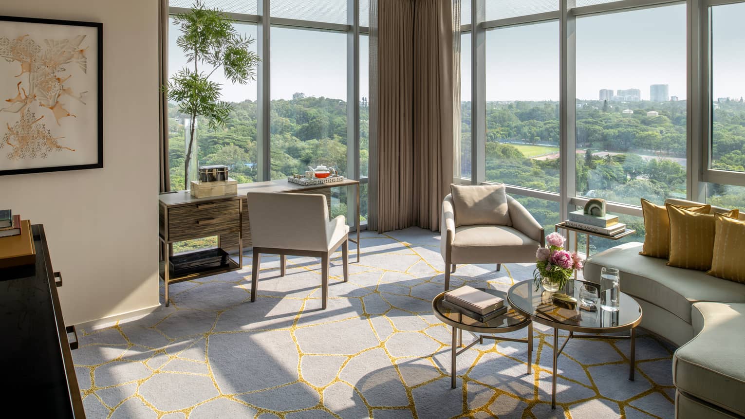 Guest room living area with cream-coloured sectional sofa and matching armchair, writing desk, gold accents, floor-to-ceiling windows