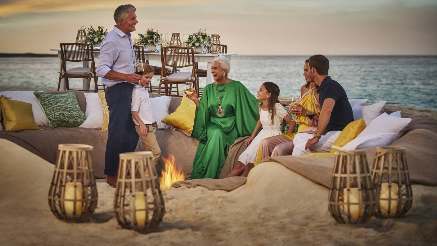 People enjoying a sunset gathering around a beach fire pit, with cozy seating and ocean view