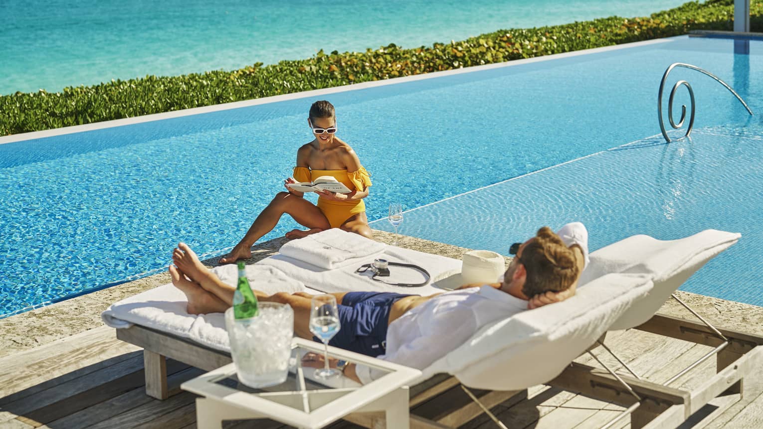 Man and woman sitting in lounge chairs by the pool.