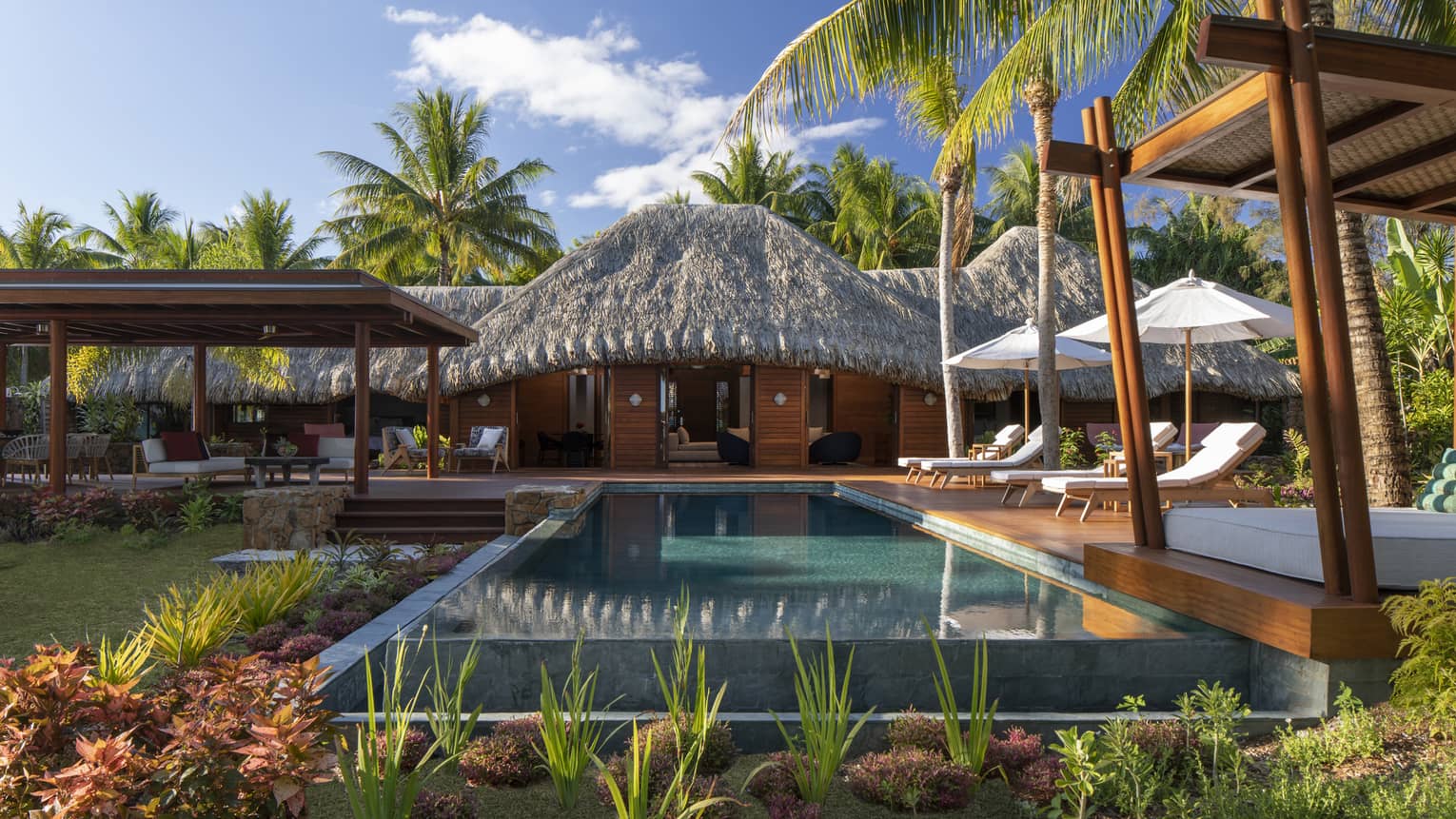 Private pool in a villa, with white sun chairs and a thatched-roof patio