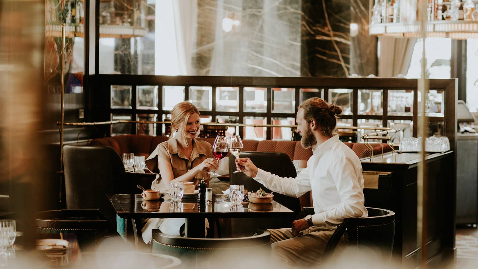 Smiling couple at table toasts with wine glasses in restaurant lounge