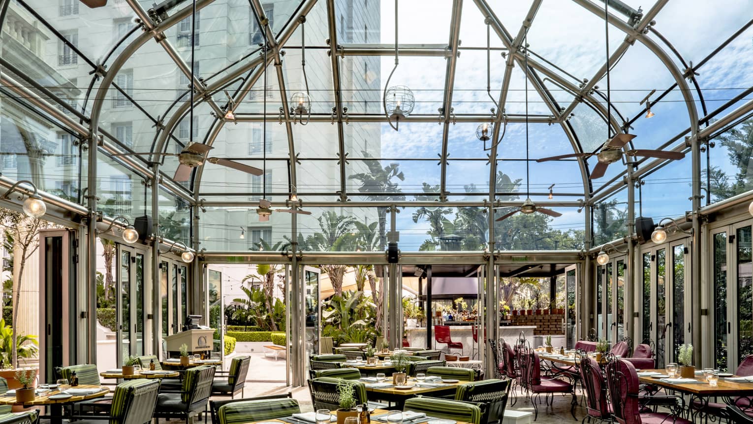 Restaurant dining room with tables set beneath a tall, retractable glass-and-metal ceiling