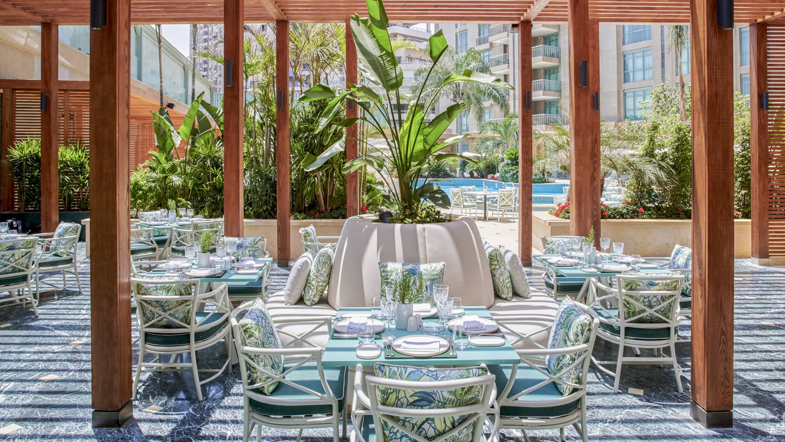 Byblos restaurant outdoor dining space with wooden columns, rattan chairs and square tables, large potted plant in middle