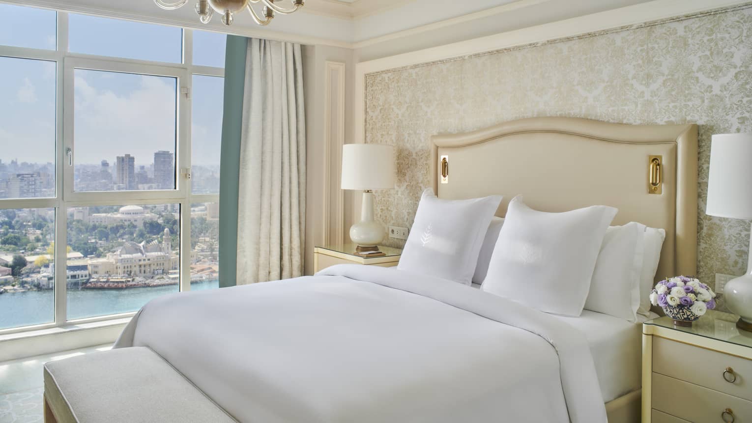 Guest bedroom with king bed, white linens and cream tufted headboard; floor-to-ceiling window with views of the River Nile