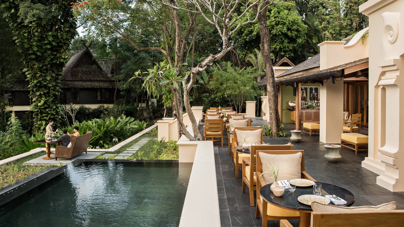 KHAO slate patio under shade of trees, long fountain by dining tables near large white columns