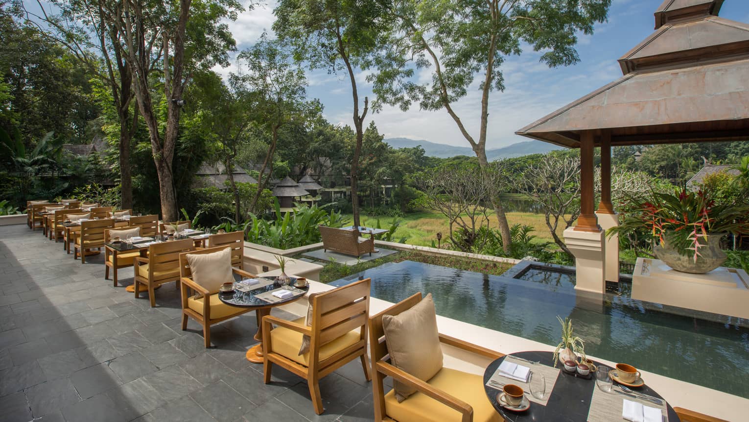 Patio dining tables line rectangular pool under wood gazebo at KHAO restaurant