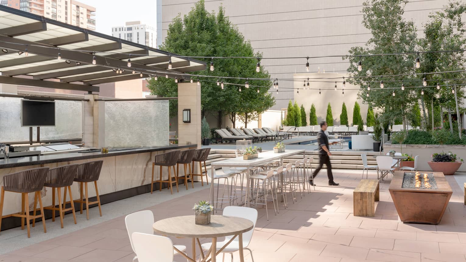 Man walks across sunny outdoor patio bar by tables, benches 