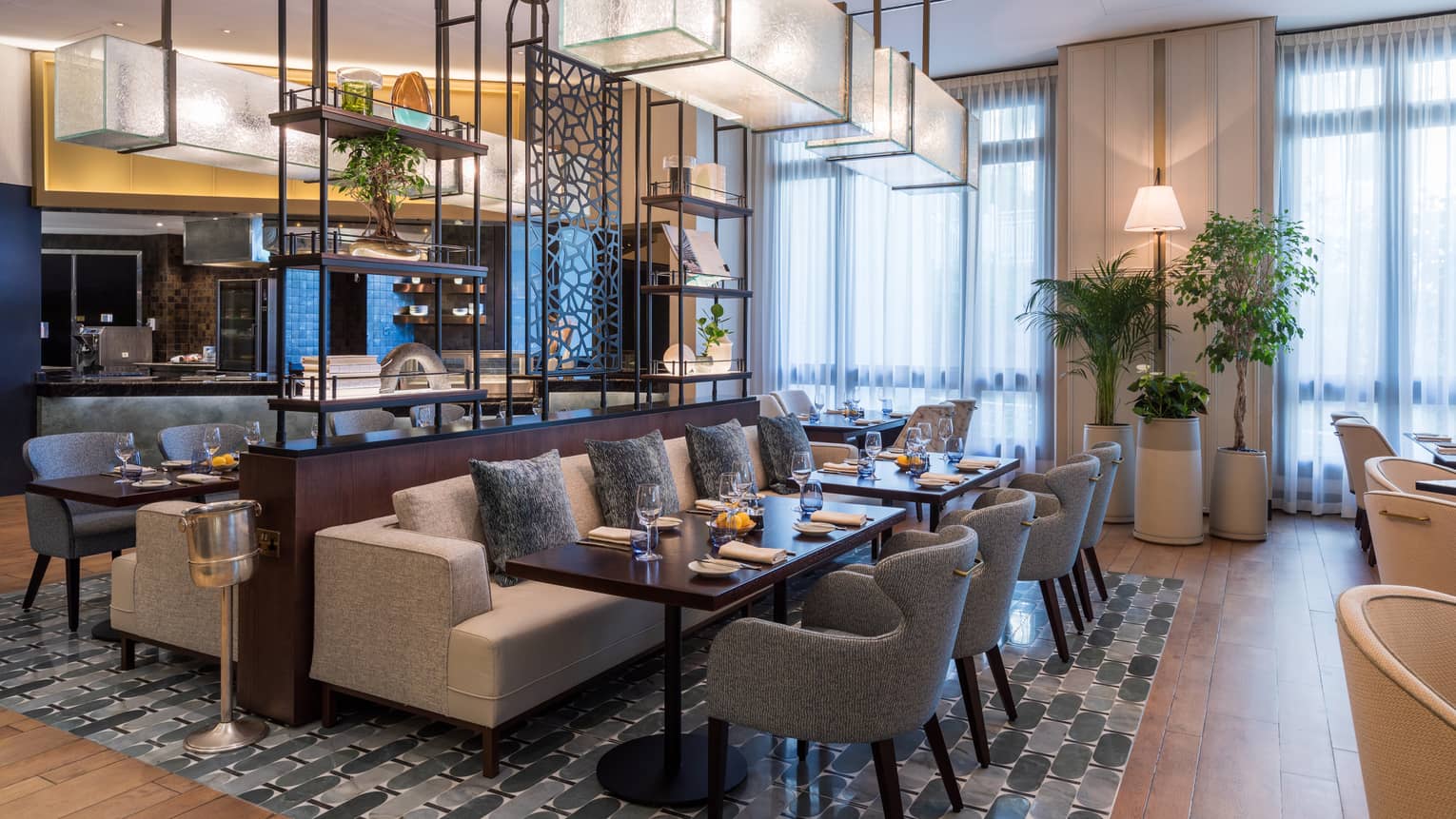 Interior of restaurant dining room with central couch-style seating mixed iwth light-blue upholstered dining chairs and rectangular glass lighting above