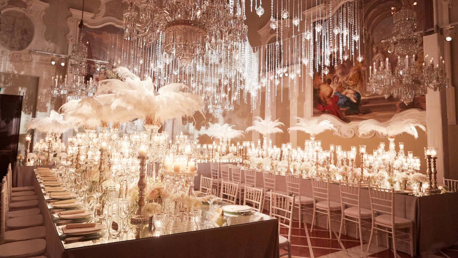 White rectangular banquet tables are decorated with tall white floral arrangements, white porcelain and glass tableware