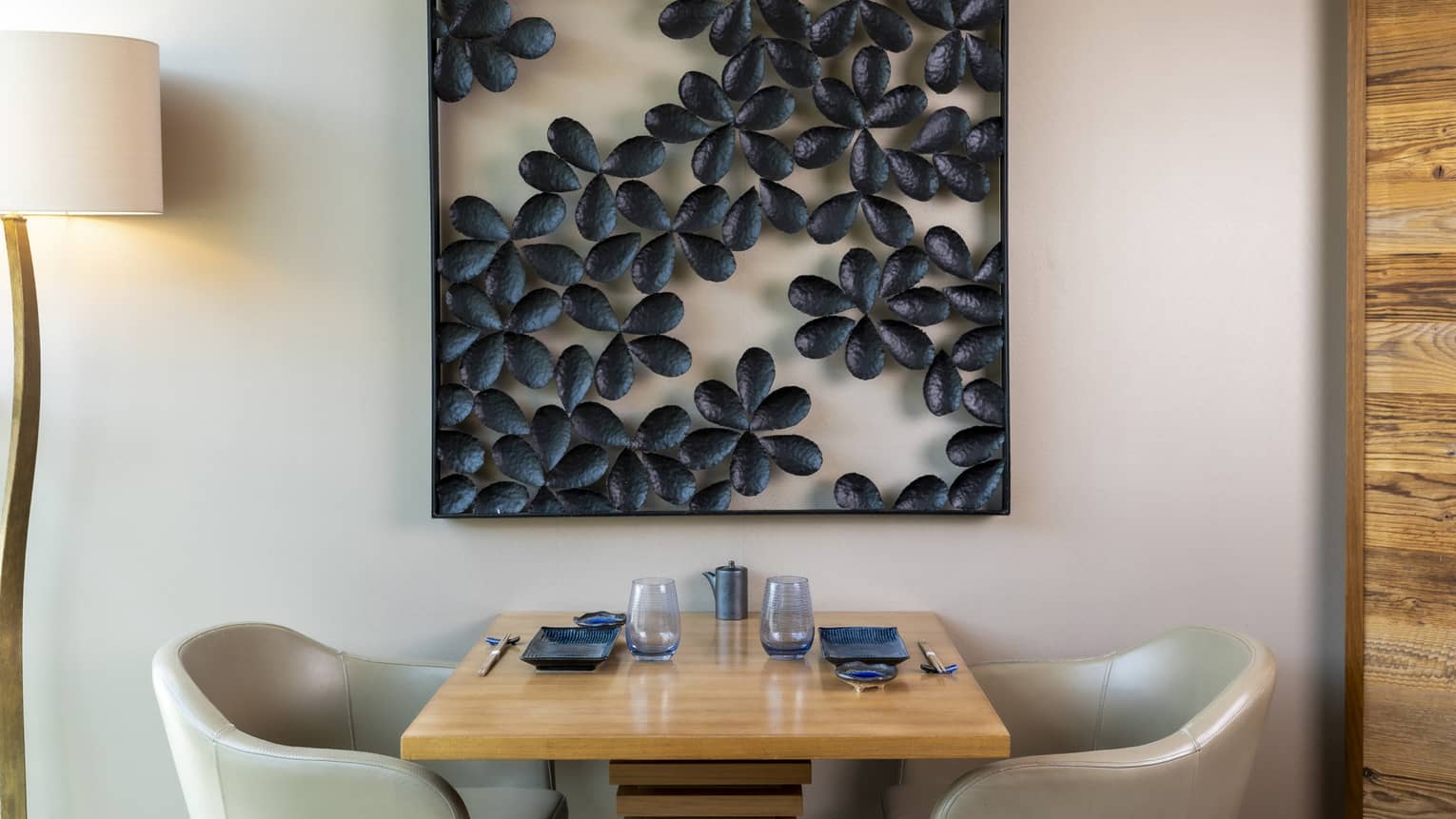 A wood dining table and two white upholstered chairs next to a wall that features a dramatic flower-themed art work.