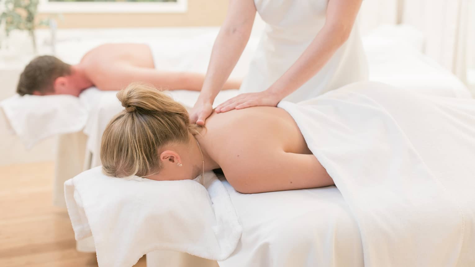 Couple laying on massage tables, spa staff massages woman's shoulders