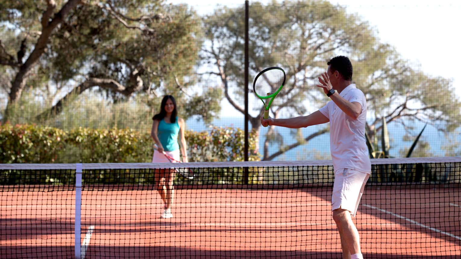 Man swing tennis racket, woman on other side of net