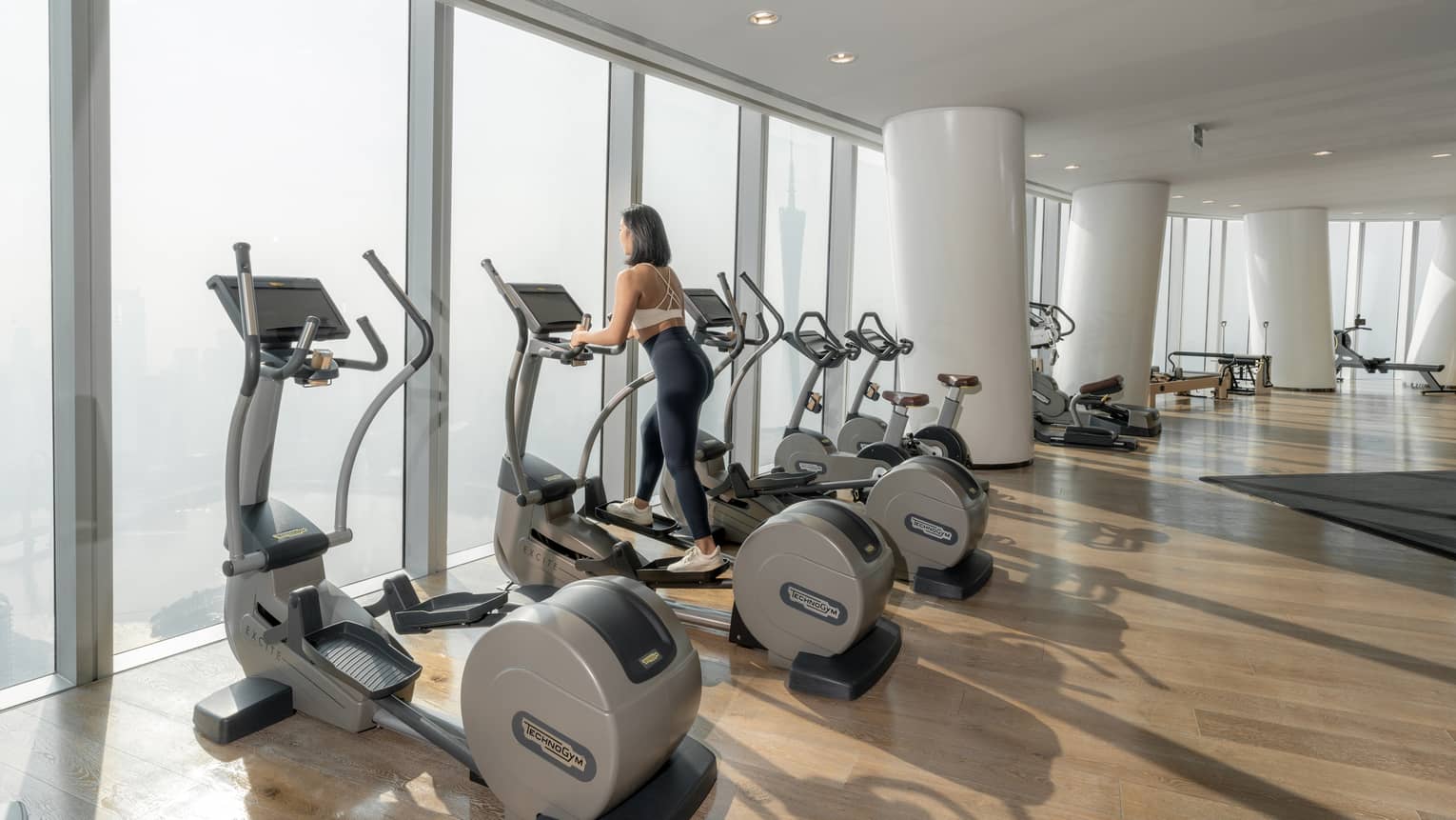 Woman on stairstepper works out in fitness room with floor-to-ceiling windows