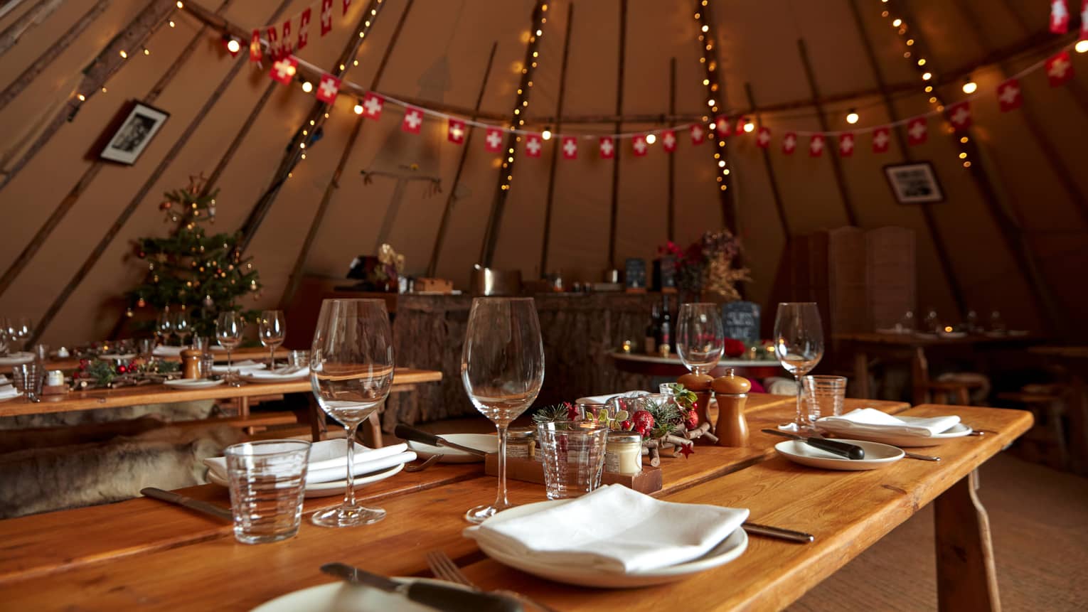 Holiday-decorated yurt with set wooden tables and string lights