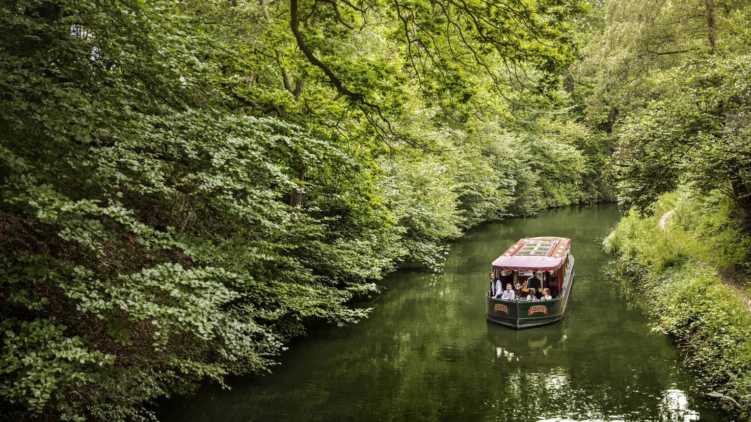 Family on canal boat Louise rides along forest-lined river 