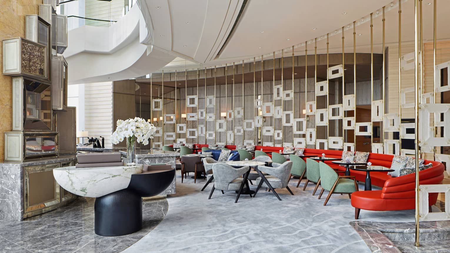 Modern lounge area with colorful seating, marble tables, decorative partition with square frames and a vase of white orchids.