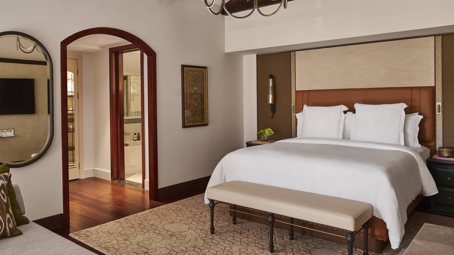 White Four Seasons bed against brown leather headboard and with neutral foot bench near arched walkway